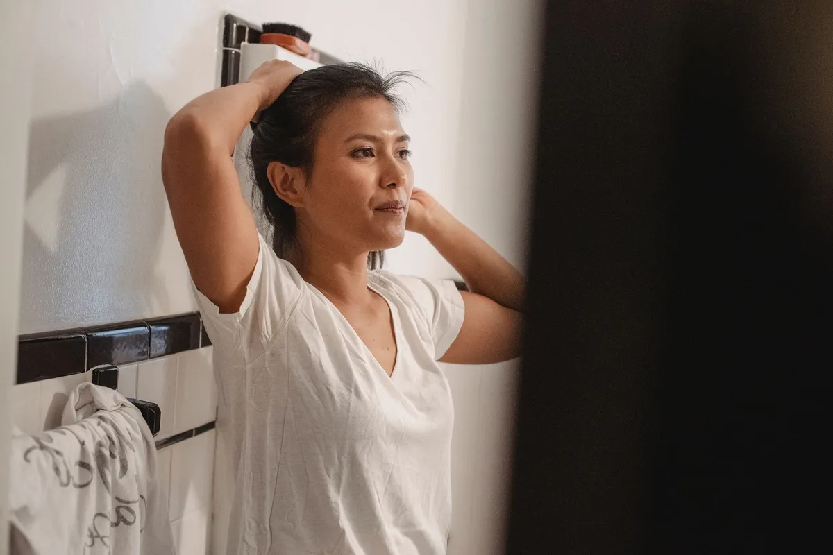 Woman drying her hair in front of a bathroom mirror