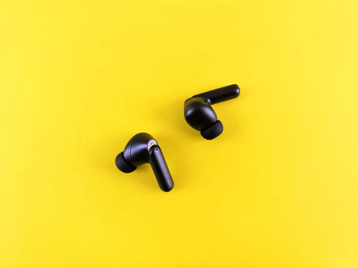 Wireless earbuds next to a pair of over-ear headphones on a desk