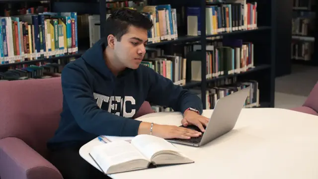 College student in over-ear headphones working on a laptop at a library table