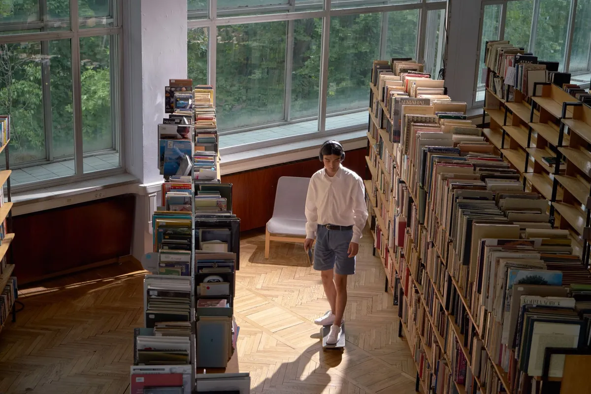 Studente con cuffie over-ear seduto al tavolo di una biblioteca