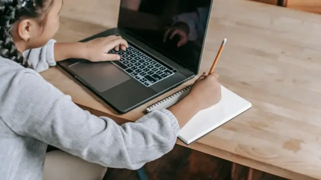 A child doing homework at a desk in front of a computer monitor